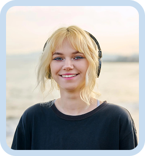 Smiling woman with blonde hair wearing headphones and a dark shirt outdoors near the water