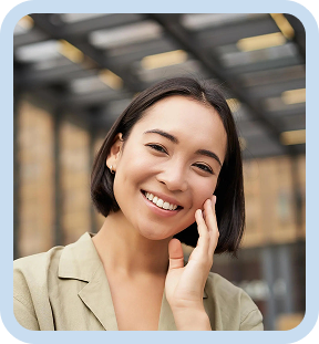 Smiling woman with short dark hair wearing a light jacket, standing outdoors near a glass building