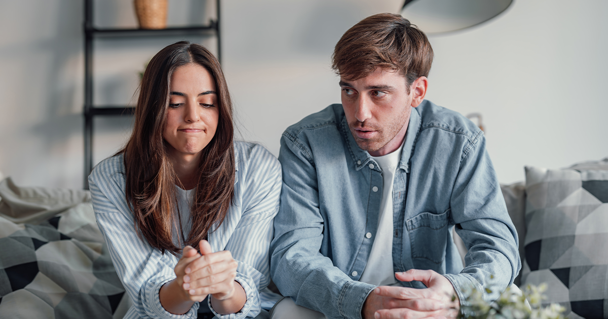 Couple sitting on a couch having a serious conversation, appearing upset or tense