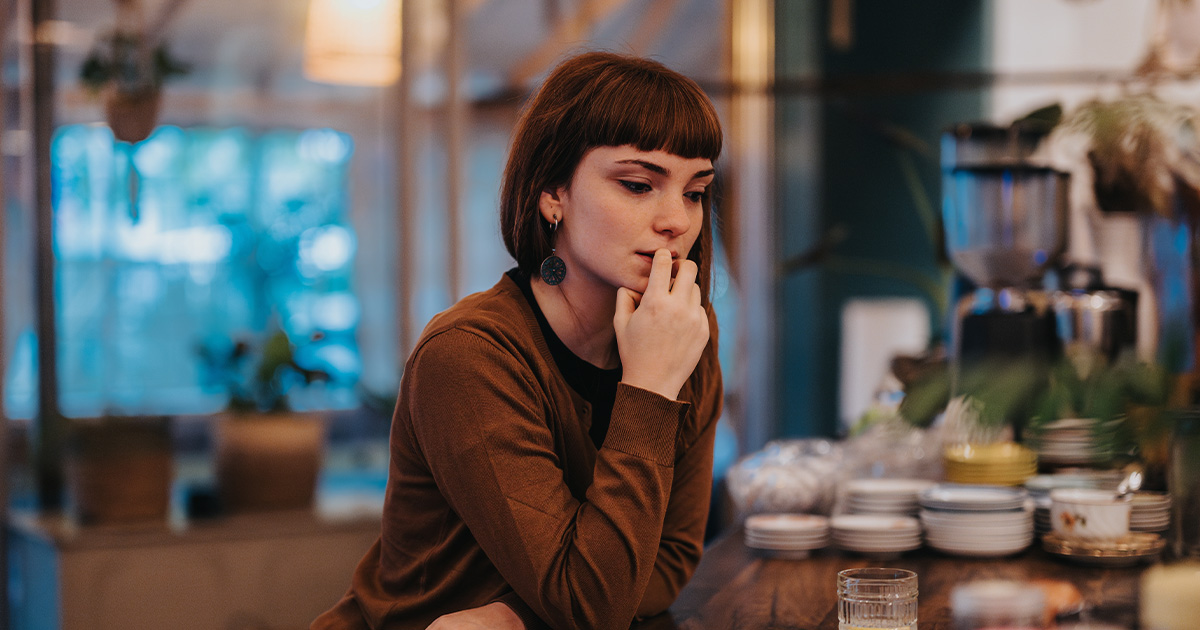 Young woman sitting at a table appearing deep in thought in a softly lit café setting