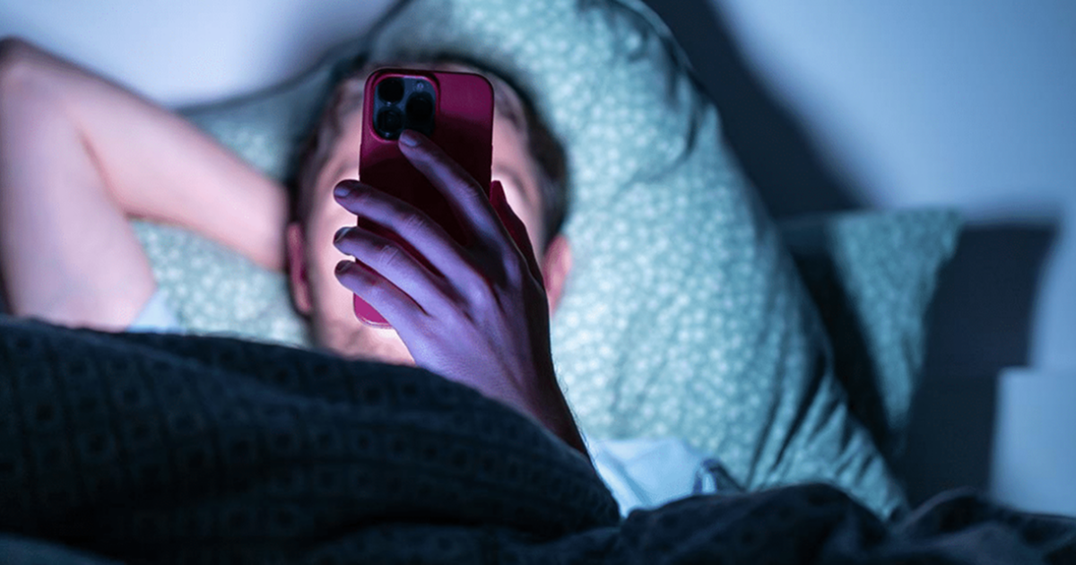 Person lying in bed at night looking at a smartphone screen in the dark