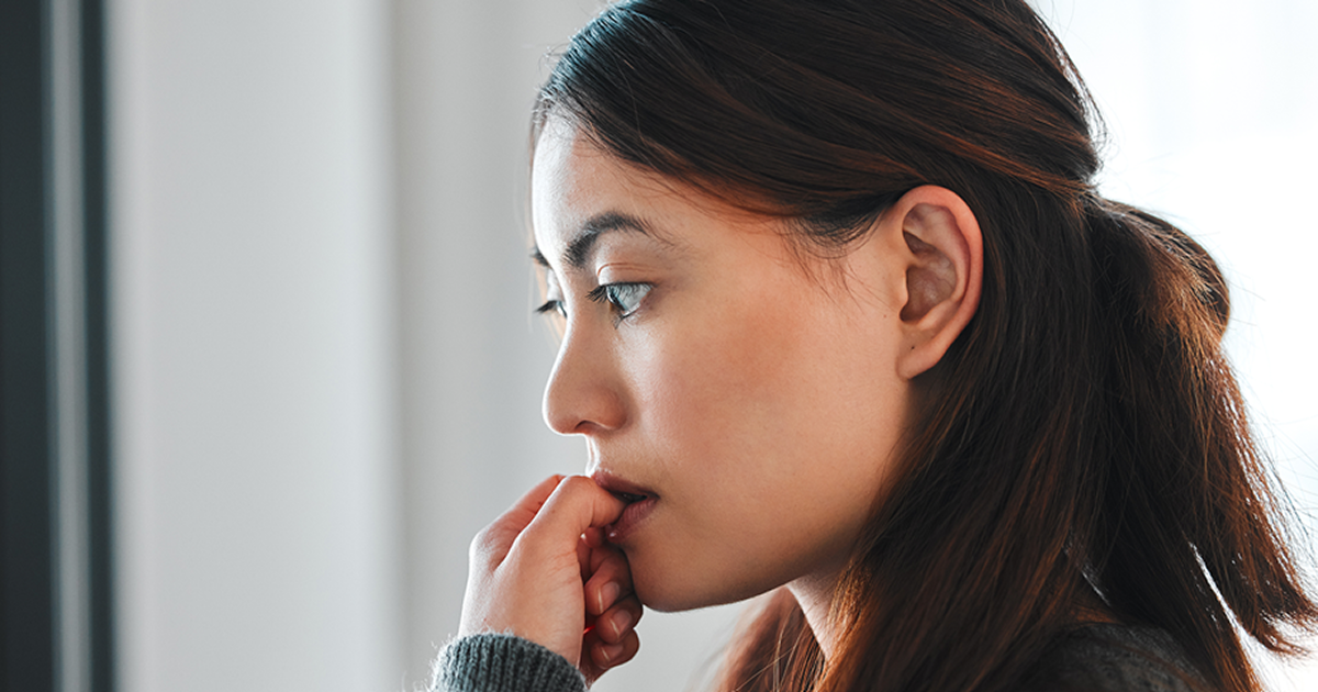 Woman looking thoughtful and anxious while resting her hand near her mouth in a bright room