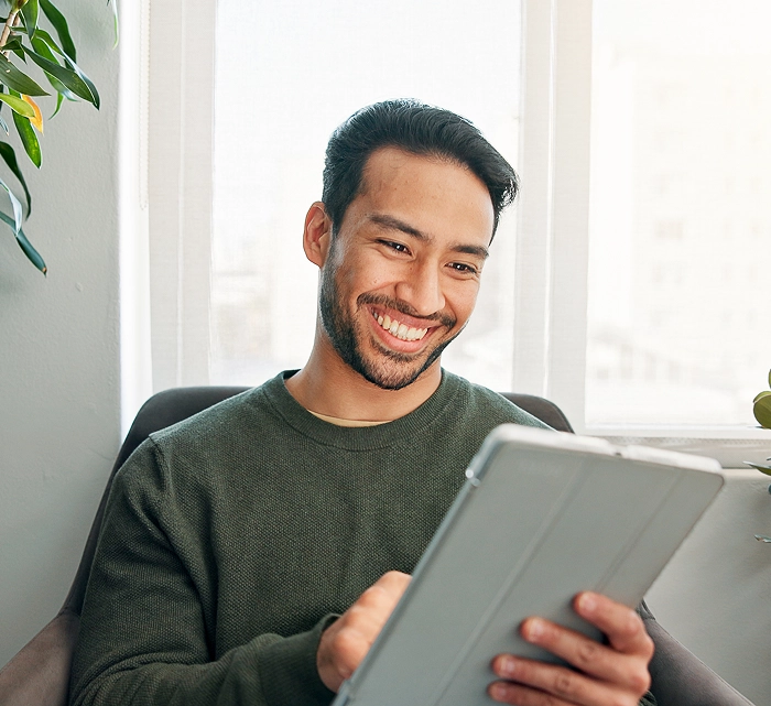 Smiling man sitting by a window using a digital tablet during an online session