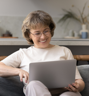 Smiling older woman sitting on a couch using a laptop at home