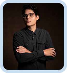 Man wearing glasses and a black button-up shirt standing with arms crossed against a dark background
