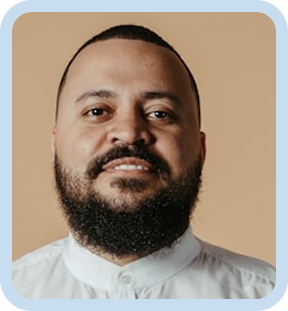 Man with short hair and full beard wearing a white shirt against a tan background