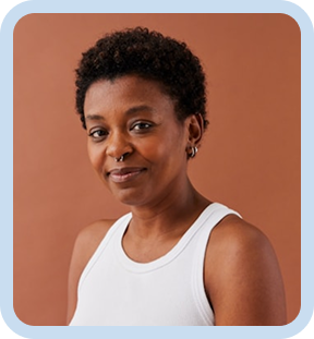 Smiling person with short curly hair wearing a white tank top against a brown background