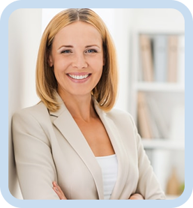 Smiling woman with blonde hair wearing a beige blazer and white top, standing with arms crossed in a bright office