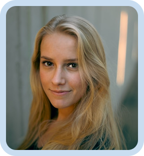 Confident woman with long blonde hair wearing a dark top, standing in soft natural light