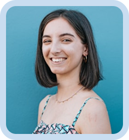 Smiling woman with short dark hair wearing a patterned top standing against a bright blue wall