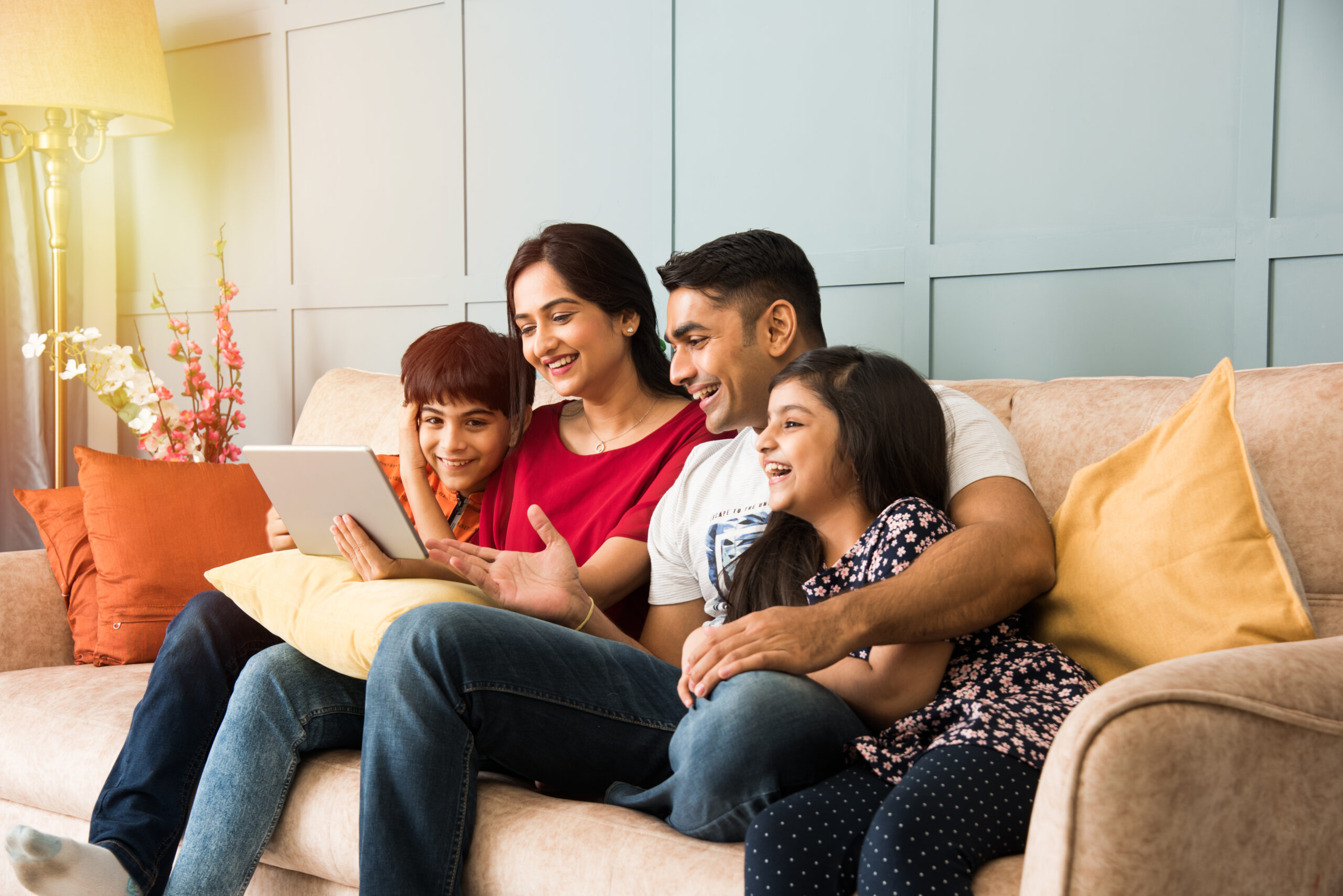 Happy family sitting on a couch smiling and looking at a tablet together at home