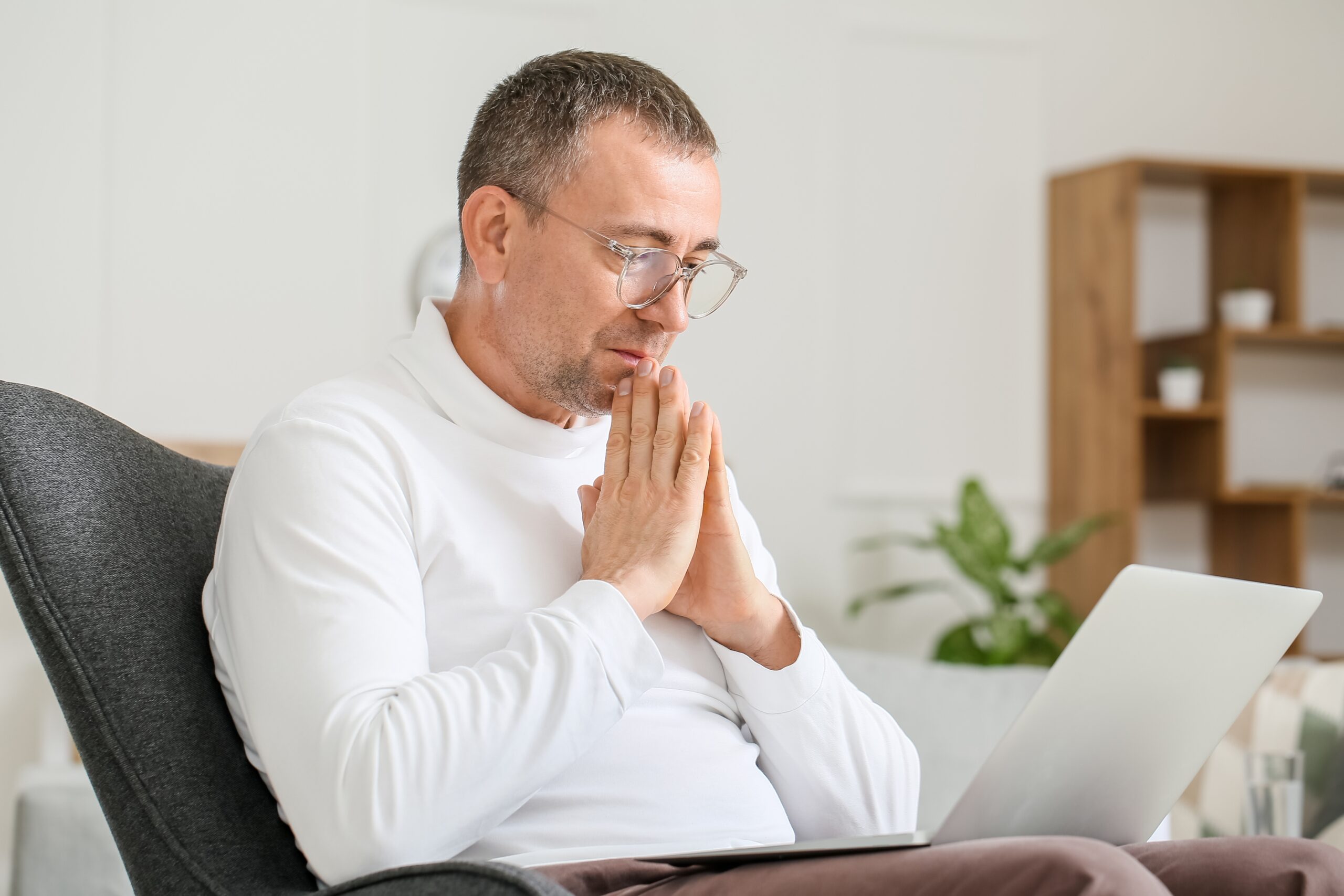 Man wearing glasses sitting at a desk looking thoughtful while viewing his laptop during a session
