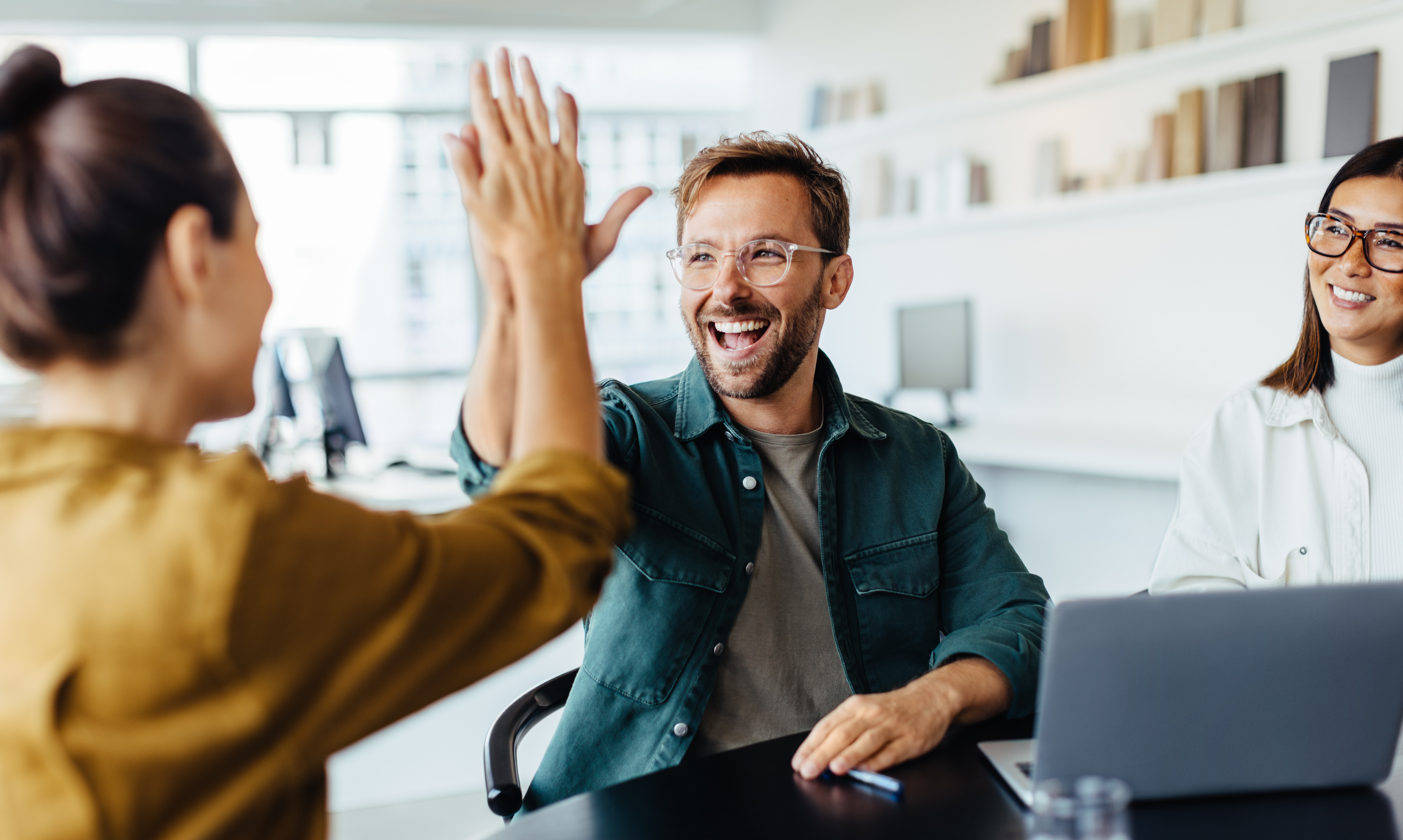 Coworkers celebrating success with a high-five during a casual meeting in a modern office