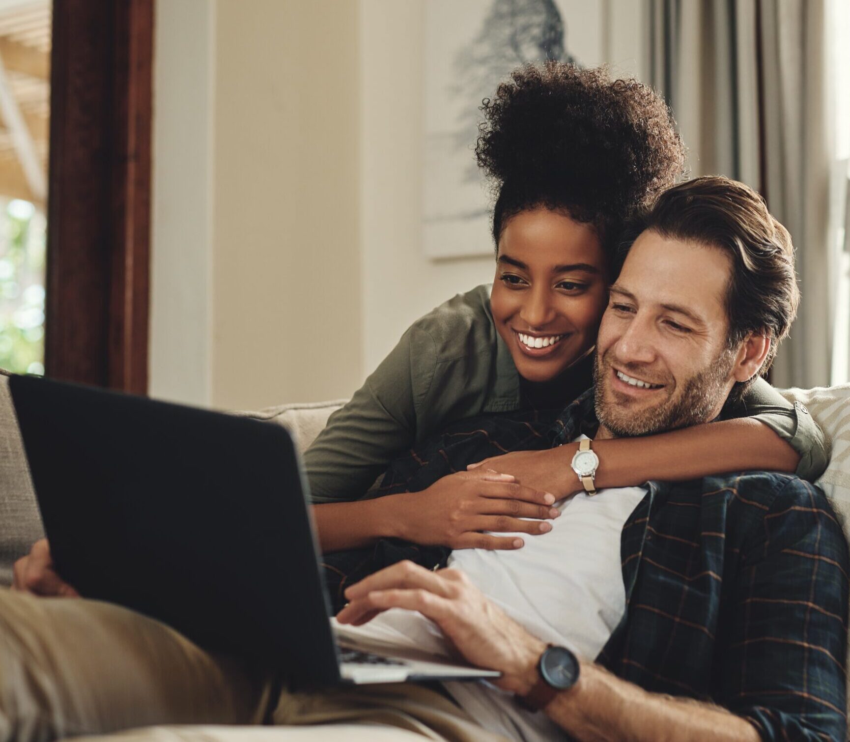 Smiling couple sitting together on a couch watching something on a laptop