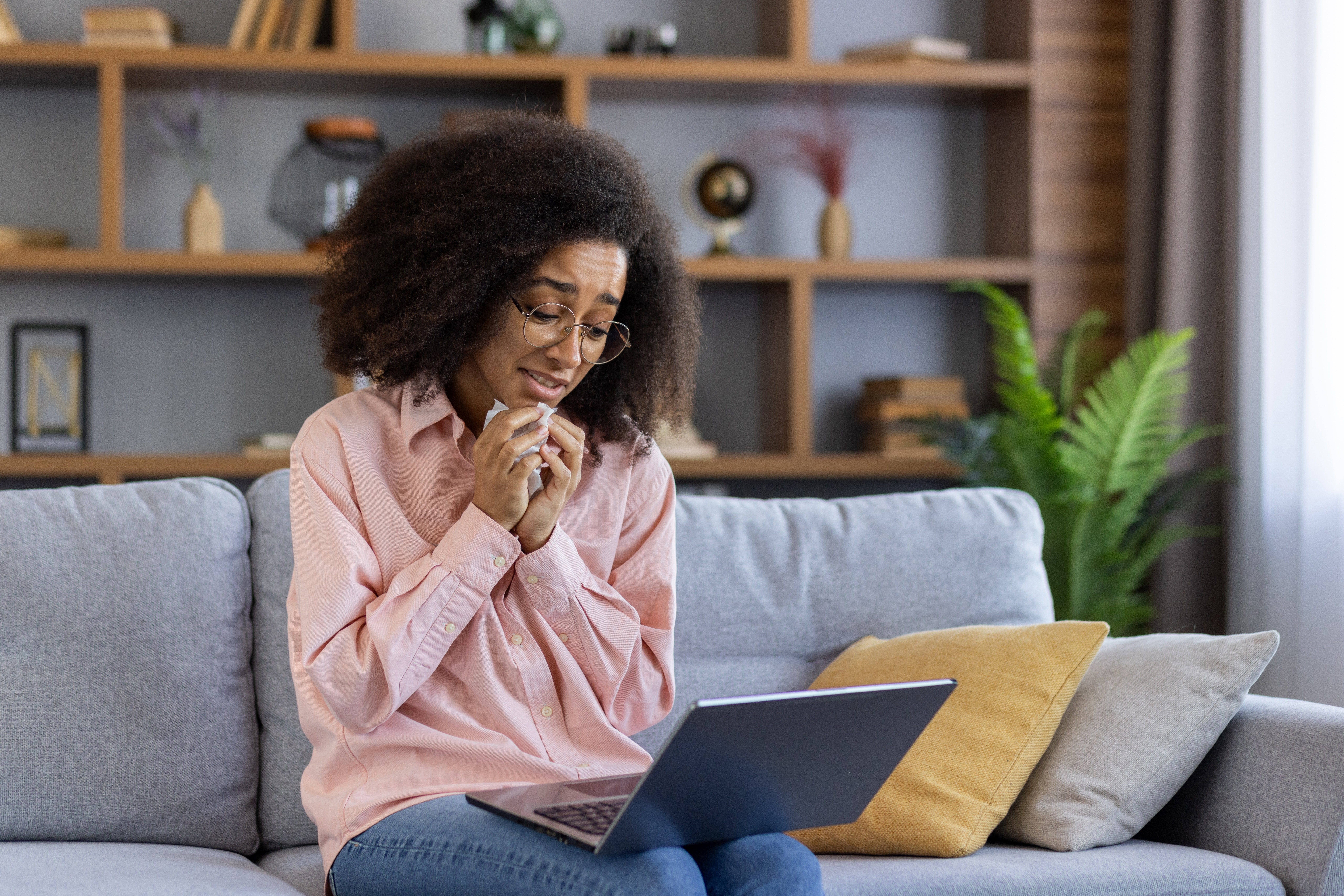 Woman sitting on a couch looking emotional while talking on a video call during an online therapy session