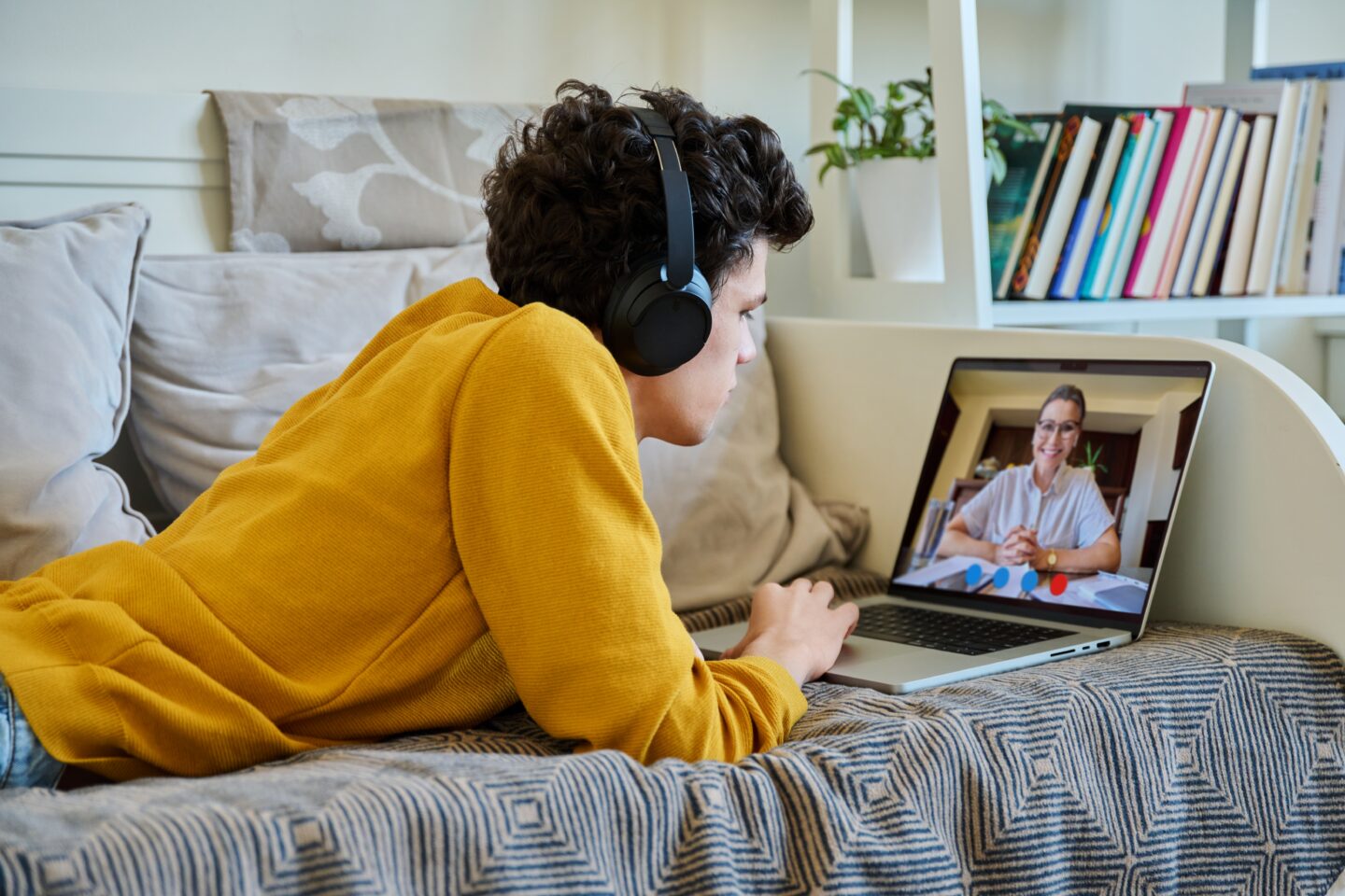 Teenager lying on a couch wearing headphones during an online therapy session on a laptop