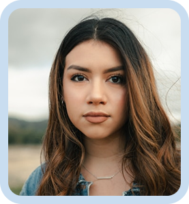 Serious young woman with long wavy brown hair wearing a denim jacket outdoors