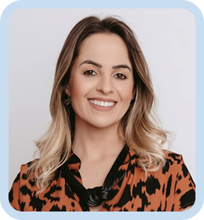 Smiling woman with wavy blonde hair wearing an orange and black patterned blouse and black necklace against light background